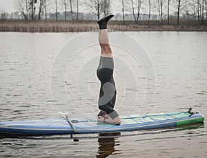 SUP YOGA, a man in a wetsuit doing yoga on a cloudy day, headstand on a paddle Board