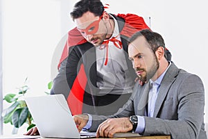 super businessman in mask and cape helping businessman with work