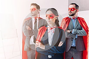 super businesspeople in masks and capes looking away with crossed arms
