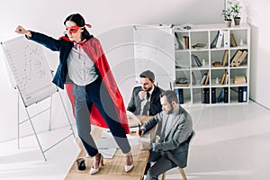 super businesswoman in mask and cape standing on table with hand up