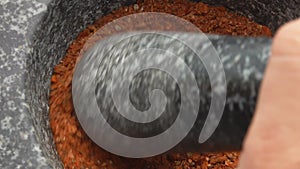 Super close-up of heavy pestle grinding spices and peppers in the stone mortar