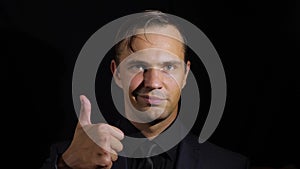 Super close-up of a man in black clothes on a black background. 4k. Slow motion. man shows thumbs up. sign super