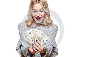 Super excited young woman in grey sweater holding bunch of Euro banknotes, celebrating winning lottery.Woman holding lots of money