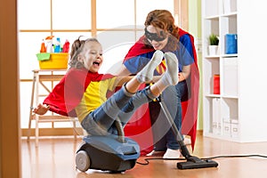 Super hero kid flying on vacuum cleaner. Mother and child daughter cleaning the room and have a fun