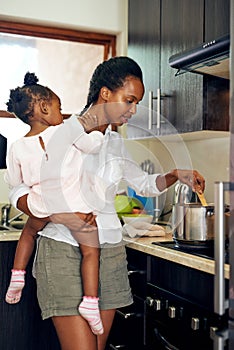 Super mom. a young mother cooking while holding her daughter in the kitchen.