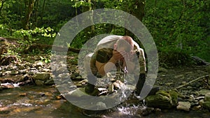 Super slow-mo. Man in khaki uniform washing his face from a forest stream with water