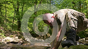 Super slow-mo. Man in khaki uniform washing his face from a forest stream with water