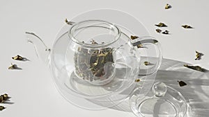 Super Slow Motion of Tea Leafs Falling in Glass Teapot on White Table