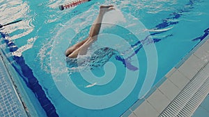 Super slow motion. Top view of skillful female swimmer while she swims backstroke style in the pool and performing