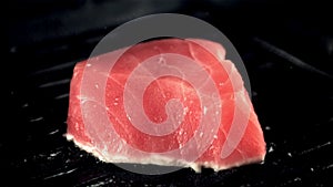 Super slow motion tuna steak is fried in a grill pan with splashes of oil. Filmed on a high-speed camera at 1000 fps.