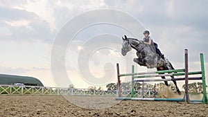 Super slow motion of a woman jockey jumps over the barriers on a horse.