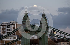 Super snow moon next to the towers of historic Hammersmith Bridge, London UK which spans the River Thames.