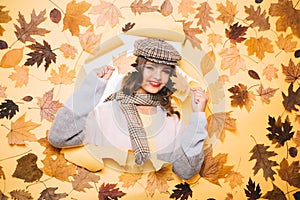 It is super warm. Fall look of vogue model. Fashion girl look through torn paper with autumn leaves. Pretty woman wear