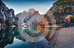 Superb autumn view of Braies Pragser Wildsee lake with boats and fishing dock.