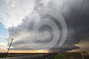 A supercell storm towers over a lonely highway in the plains.