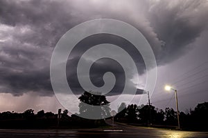 A supercell thunderstorm rotates in the sky and passes by a road intersection after sunset.