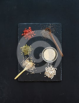 Superfoods on black chalkboard background: goji berries, chia, mung beans, buckwheat, quinoa, sunflower seeds. Top view