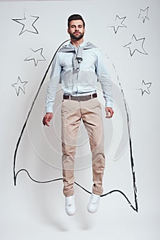 Superhero. Full length of confident bearded man wearing a drawn cape and jumping in studio against grey background with