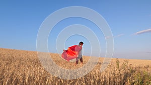 Superhero girl running across field with wheat against blue sky