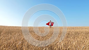 Superhero girl running across field with wheat against blue sky and smiling