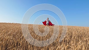 Superhero girl running across field with wheat against blue sky and smill. Slow motion