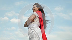 Superhero girl standing on the field in a red cloak, cloak fluttering in the wind. close-up. girl dreams of becoming a