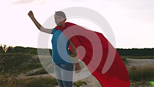 Superhero girl standing on field in a red cloak, cloak fluttering in the wind. Slow motion. beautiful girl dreams of