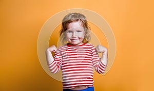 Superhero kid against yellow background. Girl power concept. Little kid girl in striped shirt