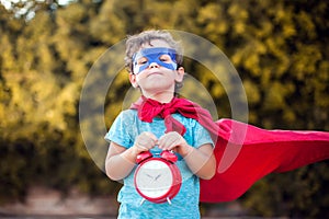 Superhero kid with alarm clock against green background outdoor. Childhood, success and and power concept