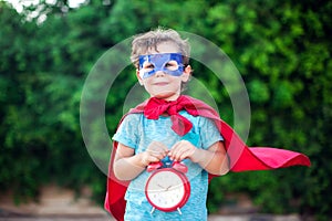 Superhero kid with alarm clock against green background outdoor. Childhood, success and and power concept