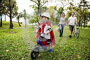 Superhero little boy riding bicycle with family in the park