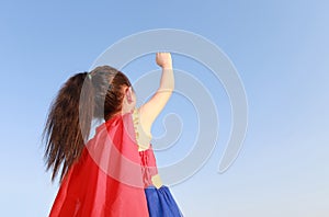 Superhero little girl in stance to fly on sky background at sunset light. Kid super hero concept. Rear view