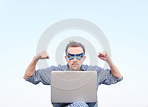 Superhero male shows strength gesture with pumped fists and laptop outdoor