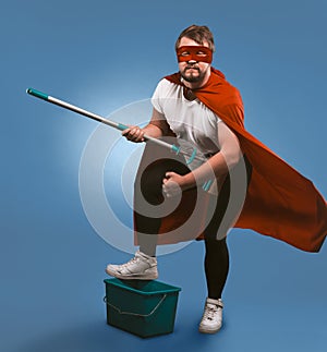 Superhero ready for cleaning work. Man in a mask and superhero red cloak posing with a bucket and a mop presenting