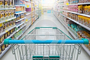 Supermarket aisle with empty blue shopping cart with customer defocus background