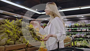 At the supermarket: beautiful young woman walks through fresh produce section, chooses vegetables and puts them in her