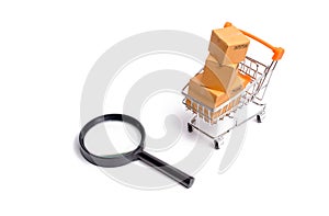 Supermarket cart with boxes, merchandise and magnifying glass: the concept of buying and selling goods and services