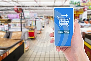 In the supermarket, close-up of a man`s hand holding a mobile phone to shop online.