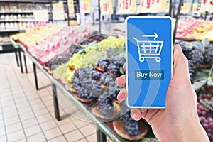 In the supermarket, close-up of a man`s hand holding a mobile phone to shop online.