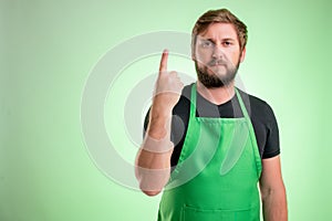 Supermarket employee with green apron and black t-shirt counting one with his finger