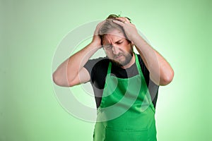 Supermarket employee with green apron and black t-shirt has headache