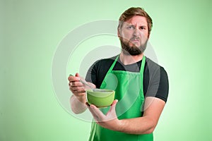 Supermarket employee with green apron and black t-shirt holding a bowl of soup that smells bad