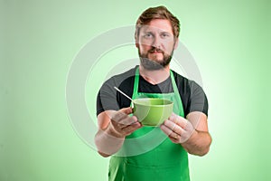 Supermarket employee with green apron and black t-shirt offers a bowl of soup