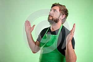 Supermarket employee with green apron and black t-shirt with open arms looking up, side view