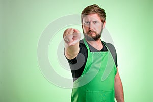 Supermarket employee with green apron and black t-shirt pointing his finger