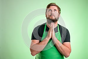 Supermarket employee with green apron and black t-shirt praying