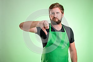 Supermarket employee with green apron and black t-shirt showing dislike