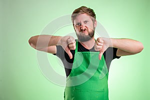 Supermarket employee with green apron and black t-shirt showing double dislike