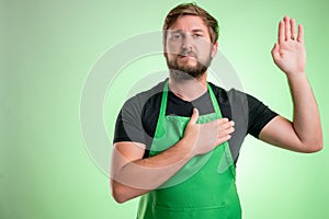 Supermarket employee with green apron and black t-shirt showing oath