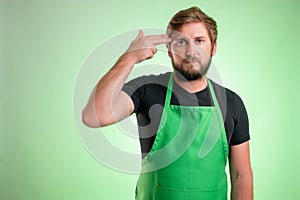 Supermarket employee with green apron and black t-shirt with showing shot head sign